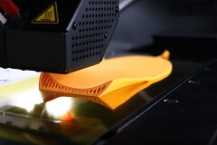 Ein 3D-Drucker fertigt die ergonomische Support-Struktur einer personalisierten orangefarbenen Einlage von Laufgsund f&uuml;r pr&auml;ventiven Halt und Stabilit&auml;t.