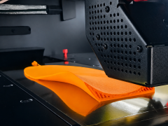 Ein 3D-Drucker stellt eine personalisierte orange Support-Einlage von Laufgsund her, basierend auf einer 2D-Druckmessung f&uuml;r ergonomischen Halt beim Gehen.