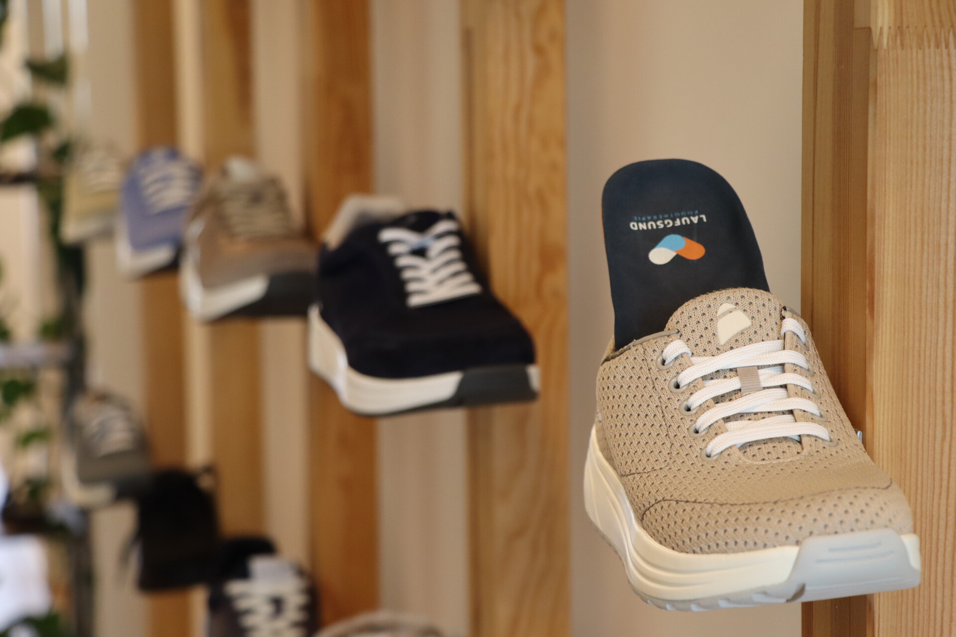 Ein beiger Anova Sneaker mit sichtbarer Laufgsund-Einlage pr&auml;sentiert auf einer Holzhalterung im Ladengesch&auml;ft &ndash; ergonomische Schuhe f&uuml;r gesundes Gehen und perfekten Halt.