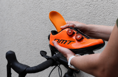 H&auml;nde schieben eine extra d&uuml;nne, orange Slimfit Support-Einlage von Laufgsund in einen Veloschuh &ndash; pr&auml;ventiver Halt und Komfort f&uuml;r enge Sportschuhe und Skischuhe.